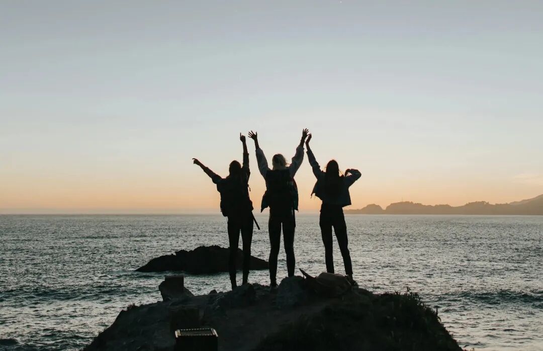 silhouette photography of persons raising hands while standing on island