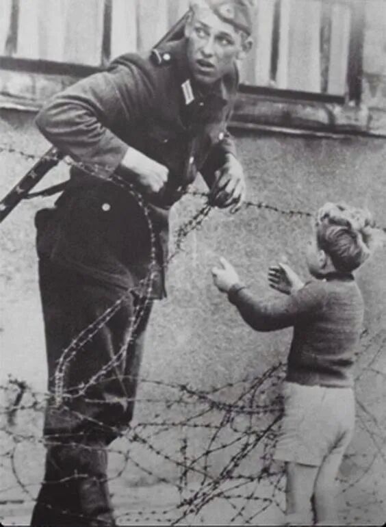 An East German soldier helping a boy cross the newly formed Berlin Wall ...