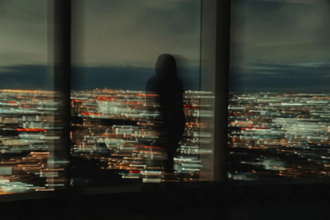 Silhouette of person looking at blurred city lights at night.