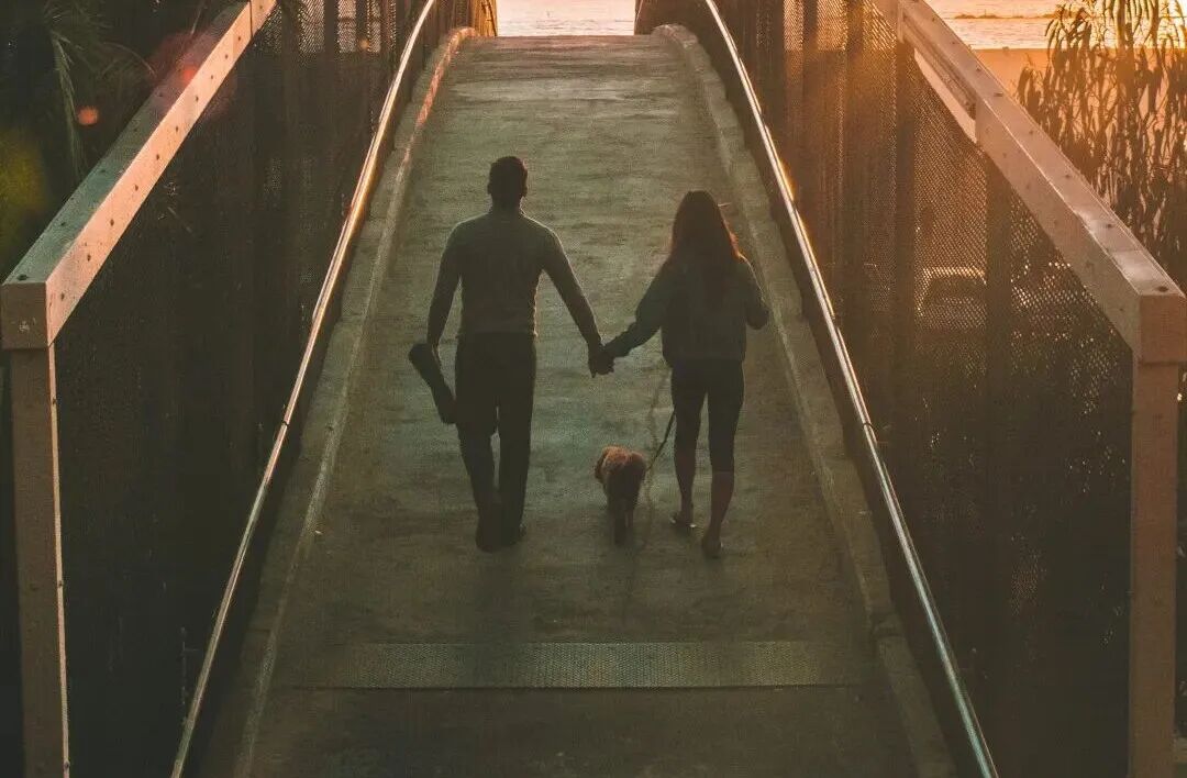 man and woman holding hand while walking on bridge