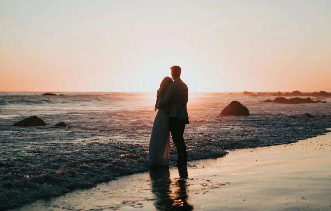 silhouette photo of couple standing on beach watching sunset