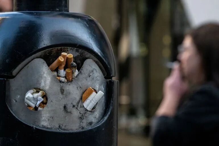 A smoker stands next to a bin for cigarette butts.