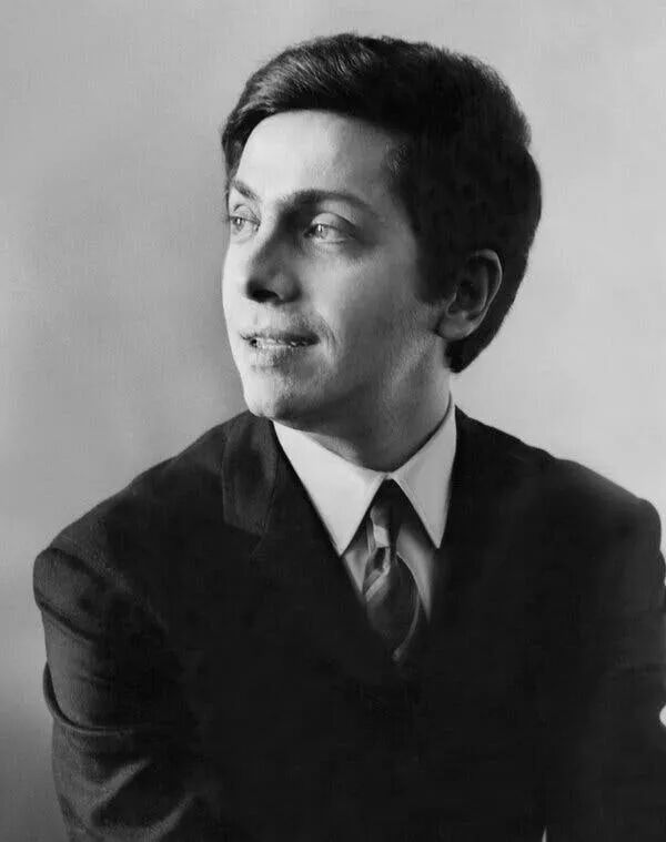 A black and white portrait of Valentino wearing a jacket, white shirt and stripped tie looking to the left with his mouth slightly open.