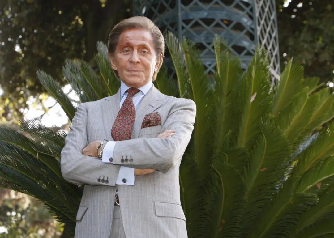 Valentino Garavani stands with arms folded.