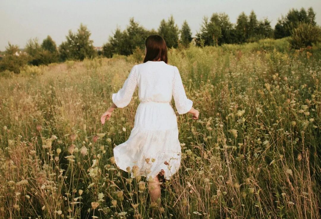 woman in white dress walking on green grass field during daytime
