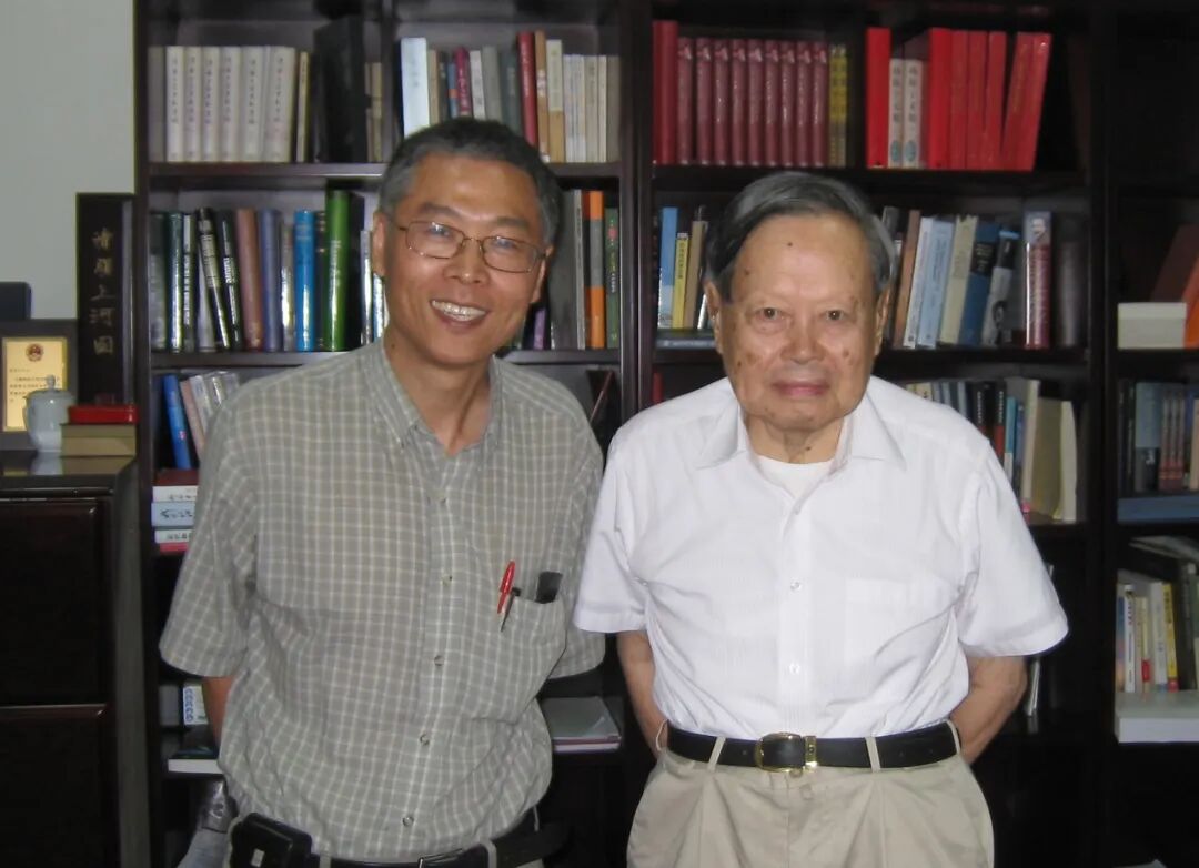 A couple of men standing in front of a bookshelf Description automatically generated