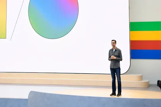 Google 和 Alphabet 的 CEO Sundar Pichai 站在台上，身后是显示渐变色“I/O”字母的背景幕。