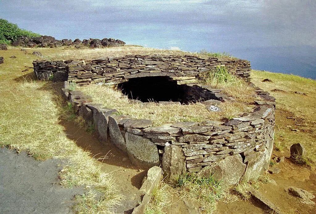 Oblong stone structure, half-covered with a flat roof and half open-air. The structure is clearly very old and grass has grown on top of and around it.